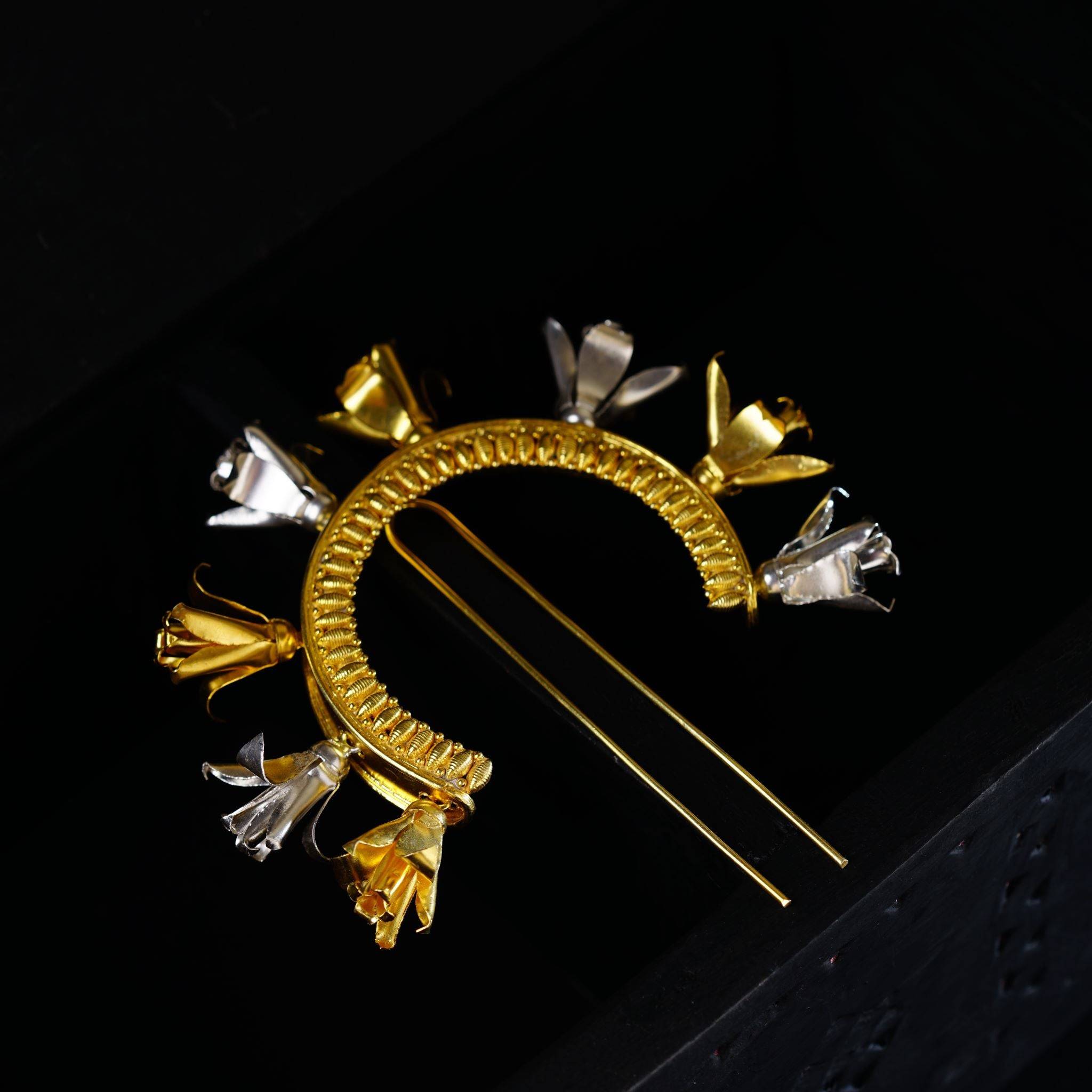a gold and silver brooch sitting on top of a black box