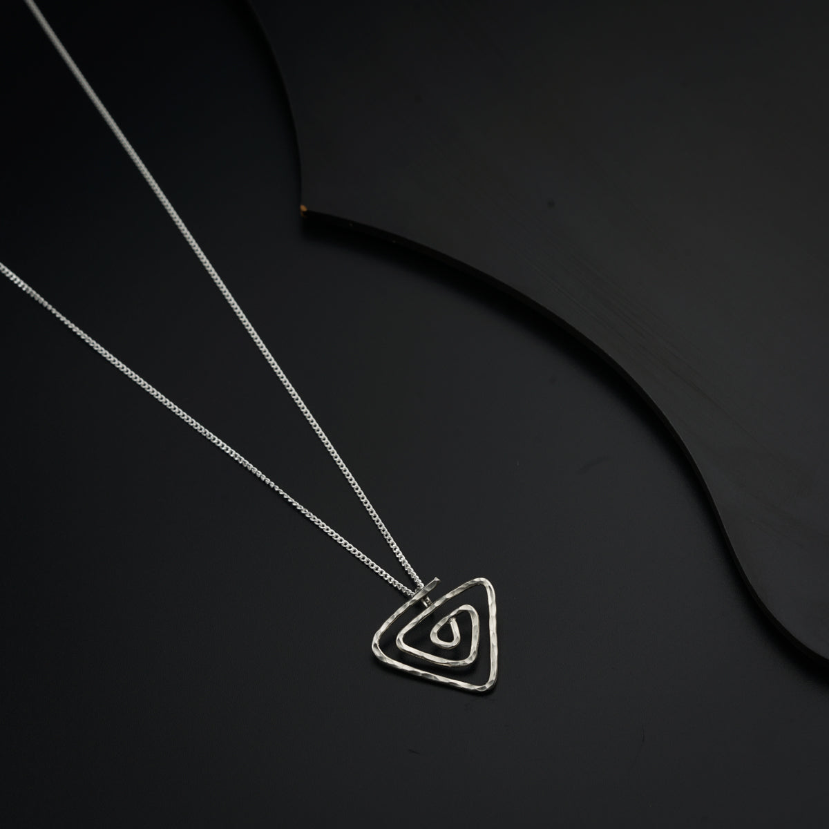 a silver necklace with a triangle on a black background