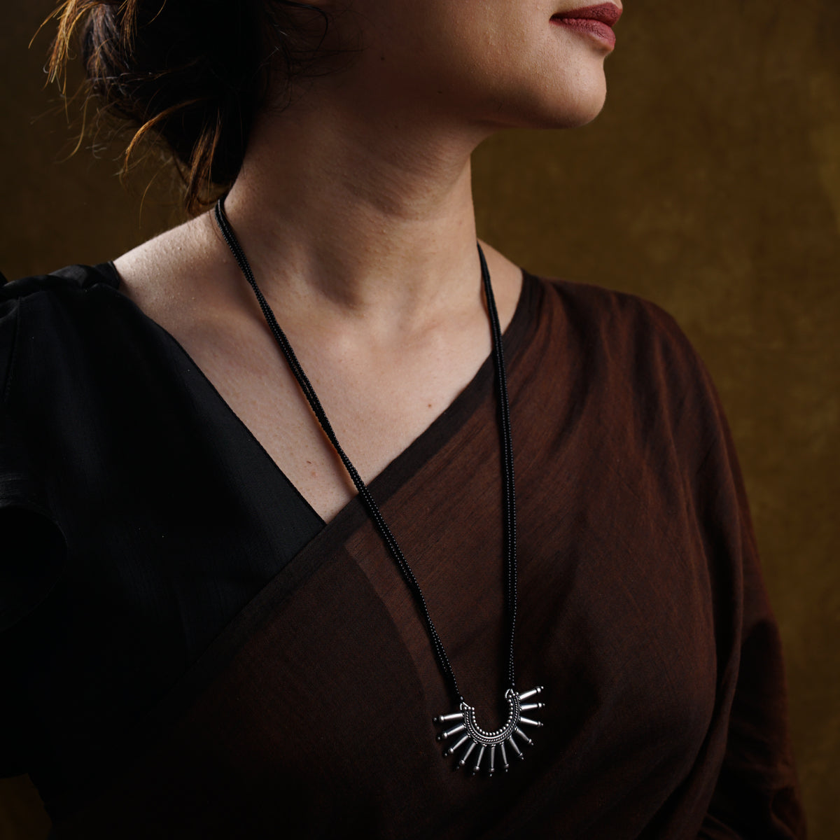 a woman wearing a brown shirt and a black necklace