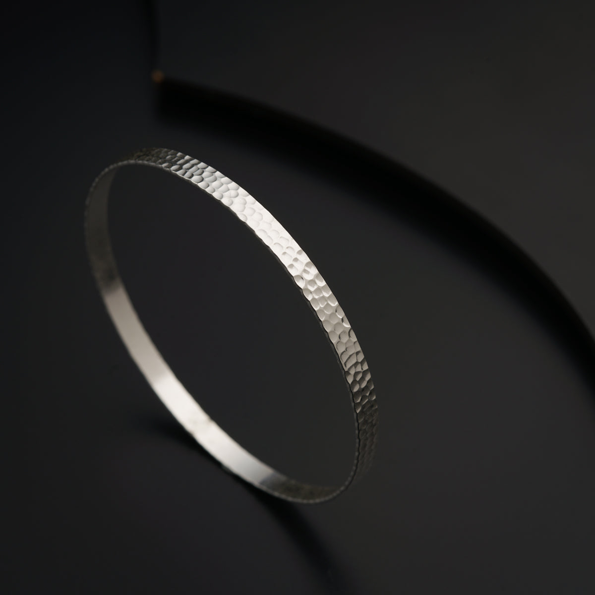 a thin silver bracelet on a black surface
