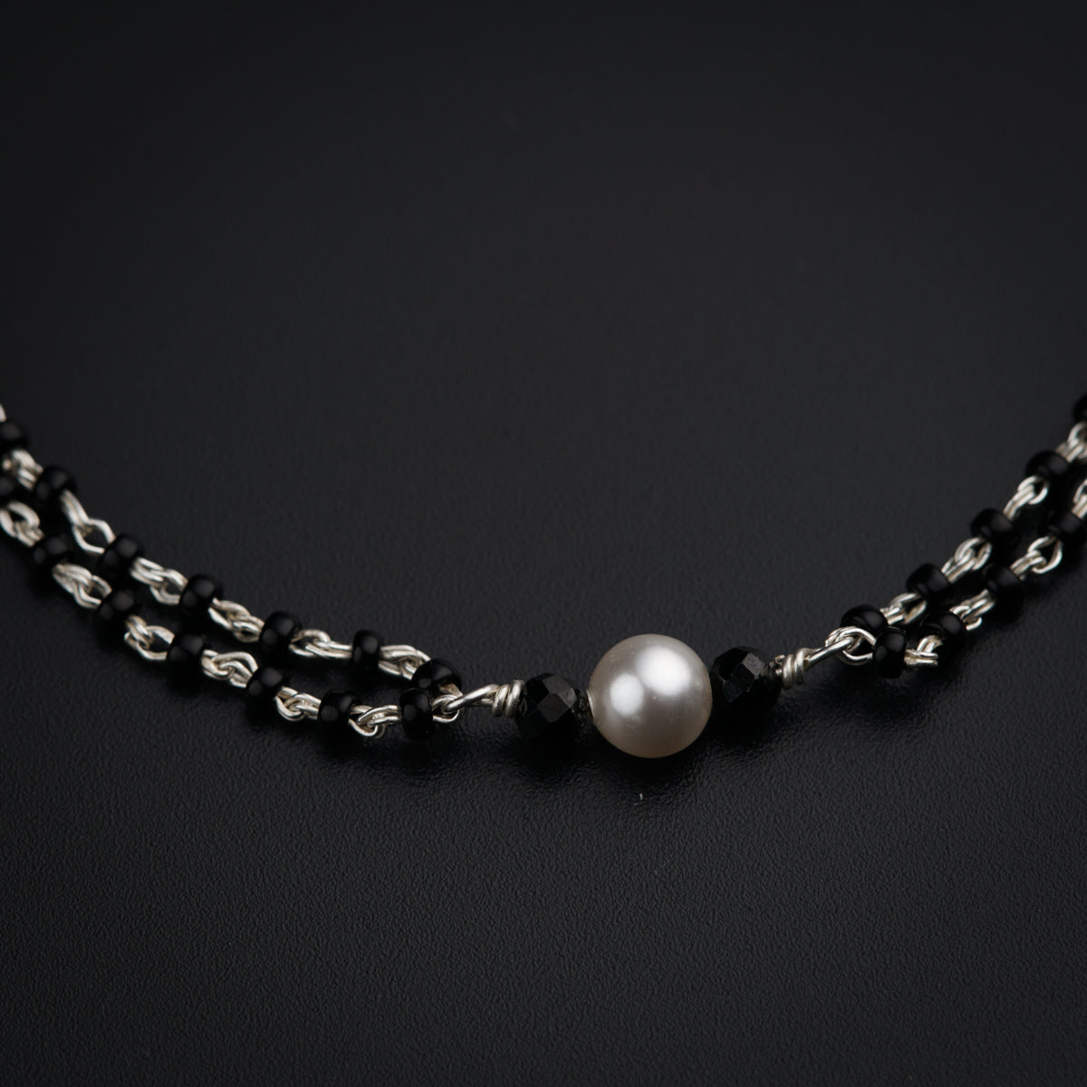 a black and silver necklace with a white pearl