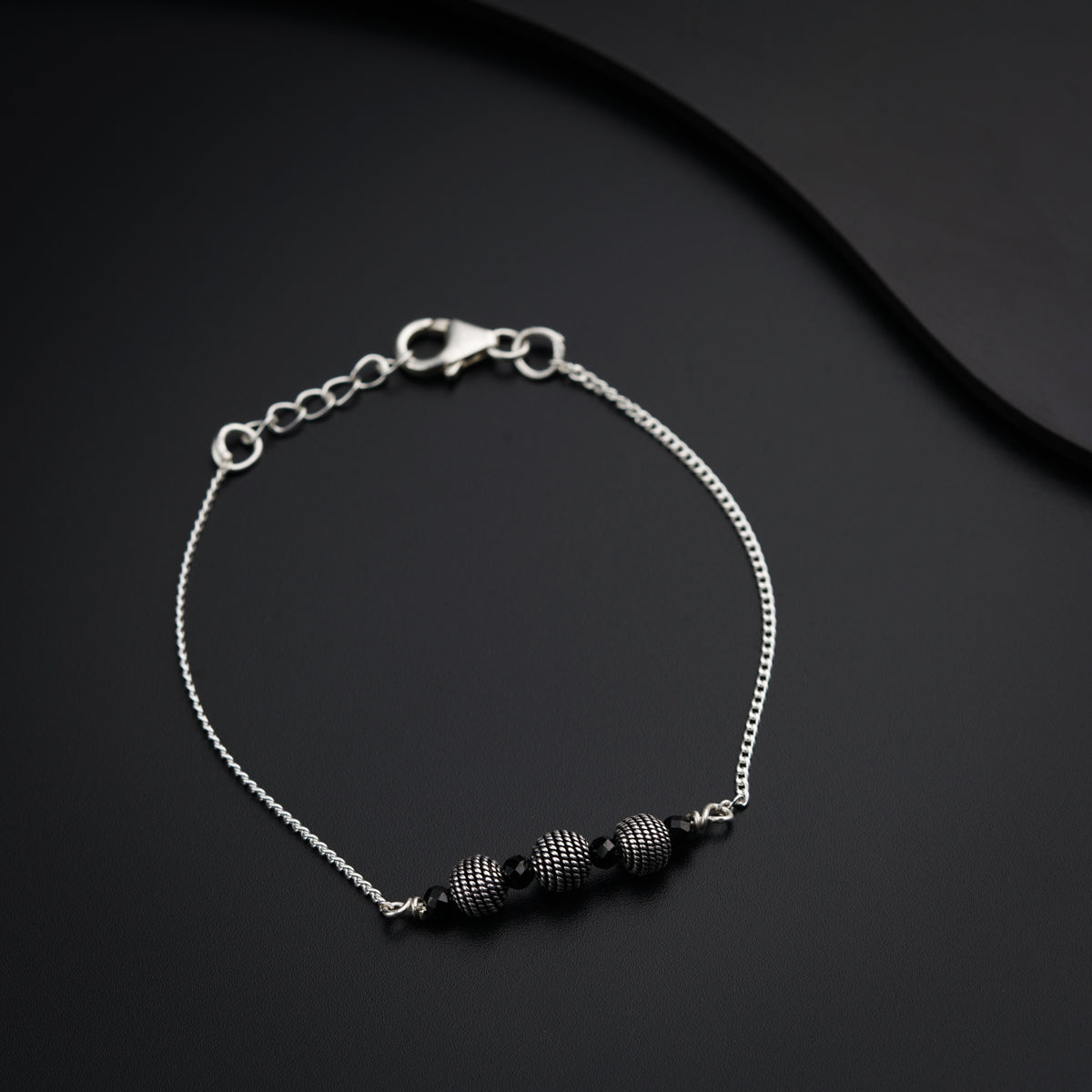 a silver bracelet with black beads on a black surface