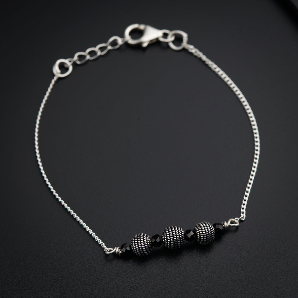 a silver bracelet with black beads on a black surface