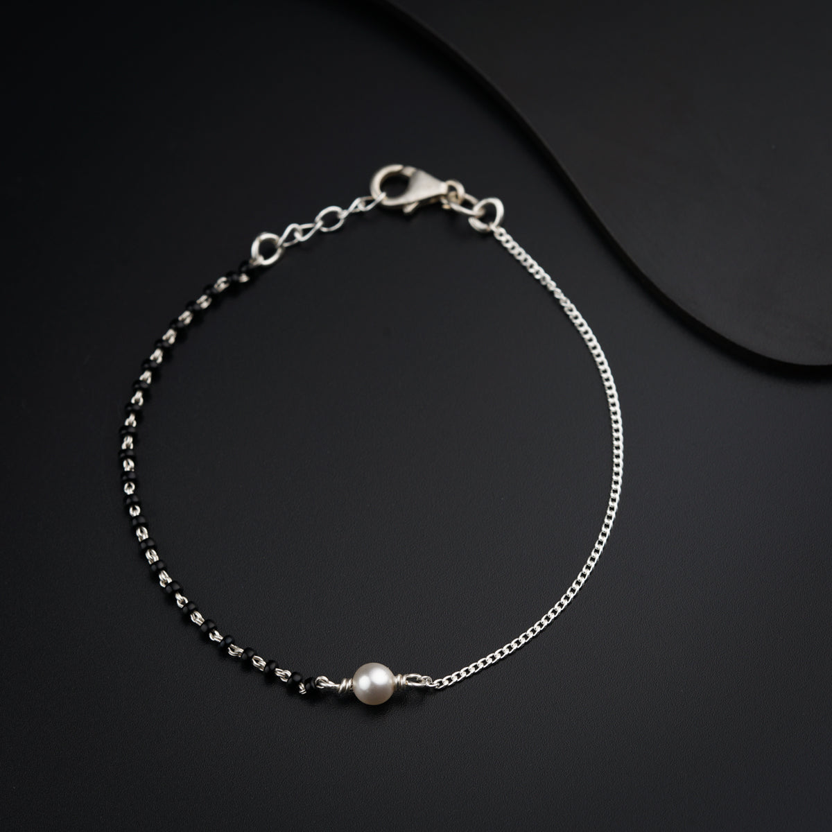 a silver bracelet with a pearl on a black background
