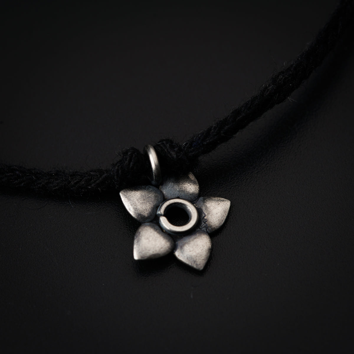 a silver flower pendant on a black cord