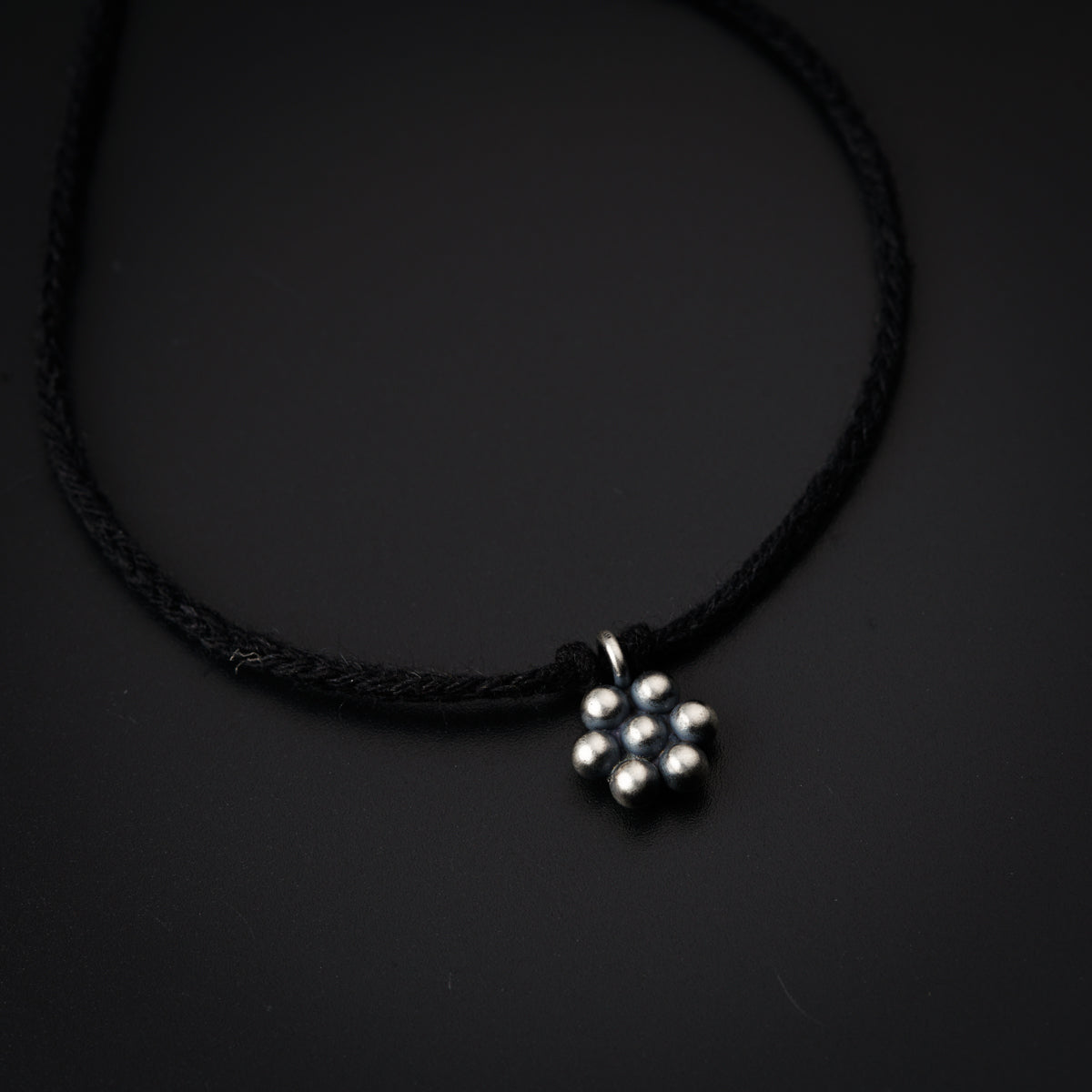 a black cord necklace with a silver flower on it
