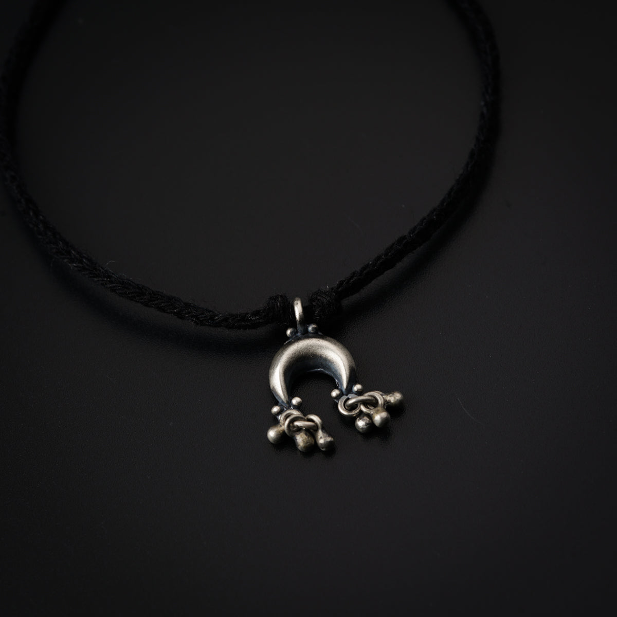 a black cord necklace with a silver pendant on it