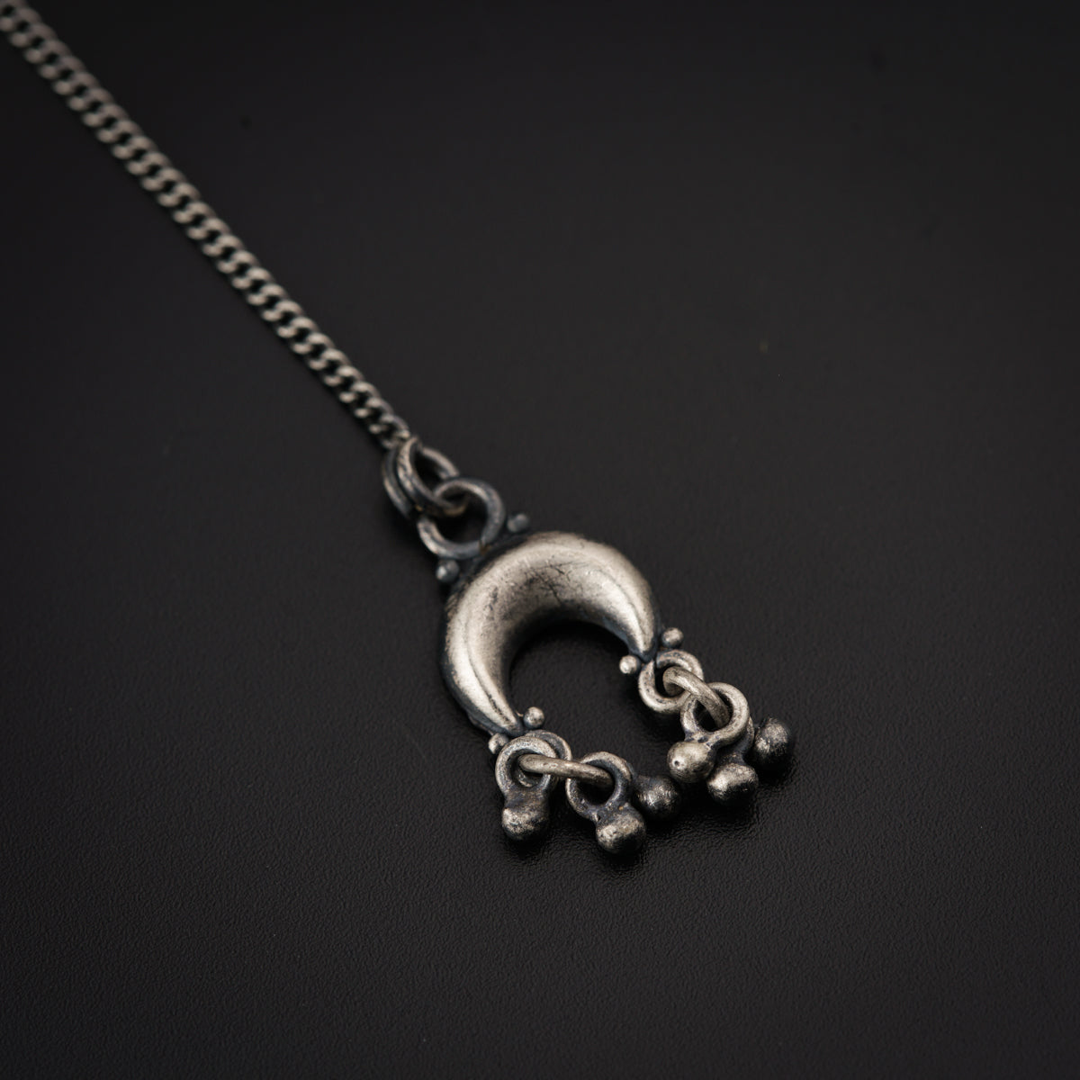 a silver necklace with a crescent on a black background