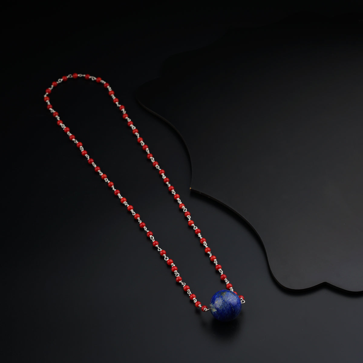 a red beaded necklace with a blue bead on a black background