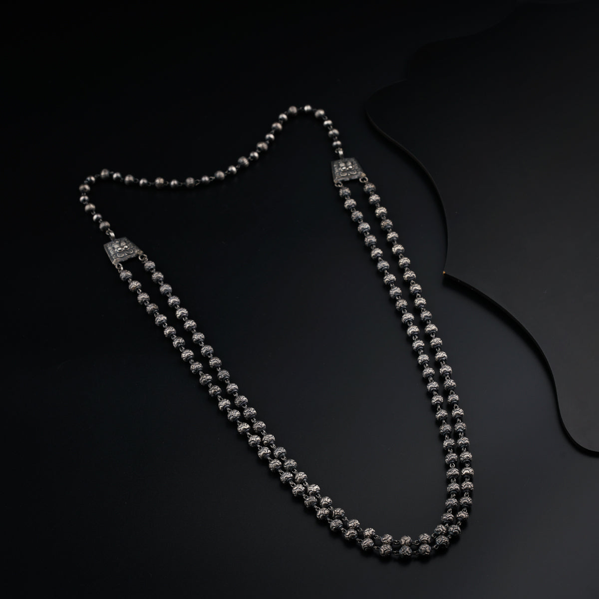 a long silver beaded necklace on a black surface