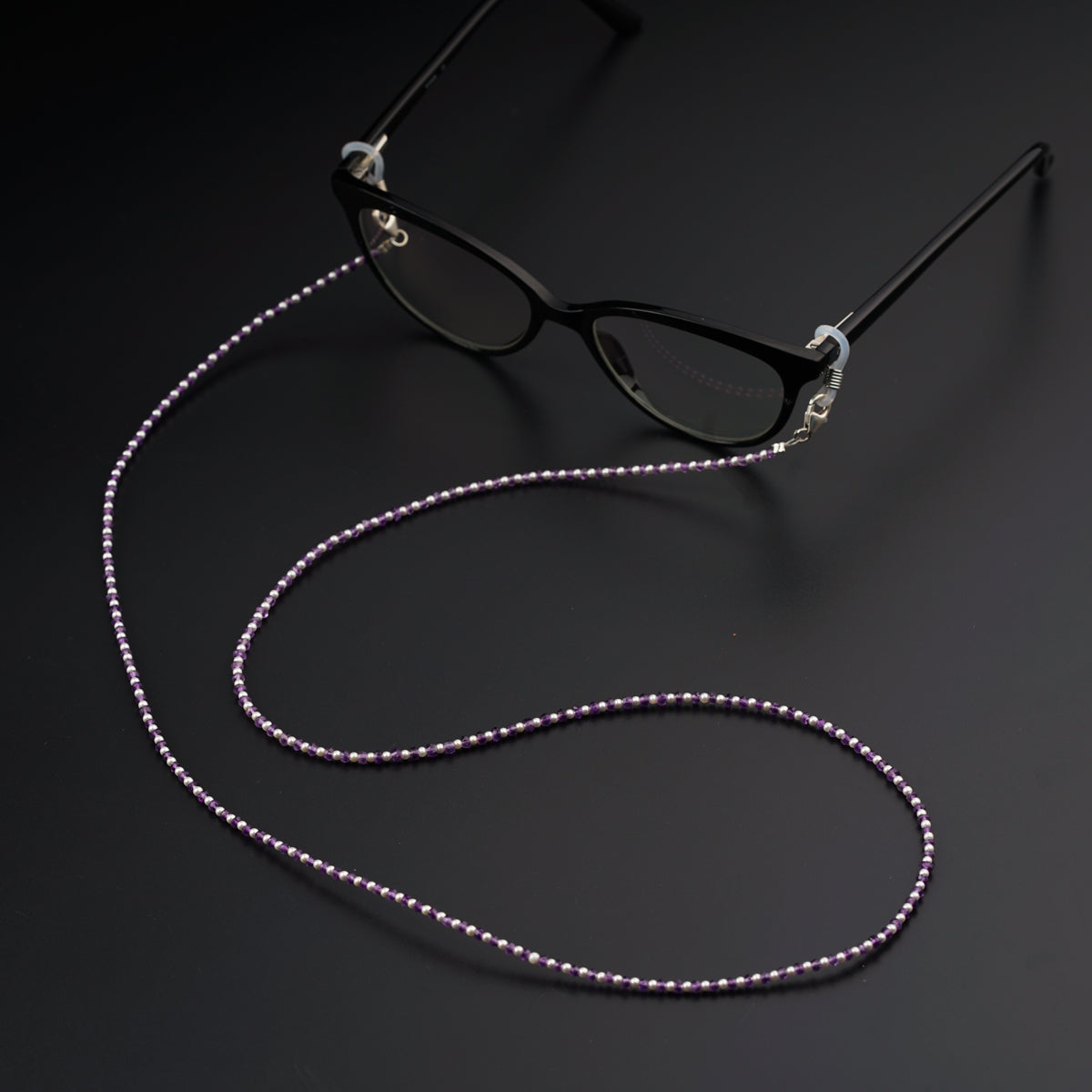 a pair of glasses and a beaded lanyard on a black surface