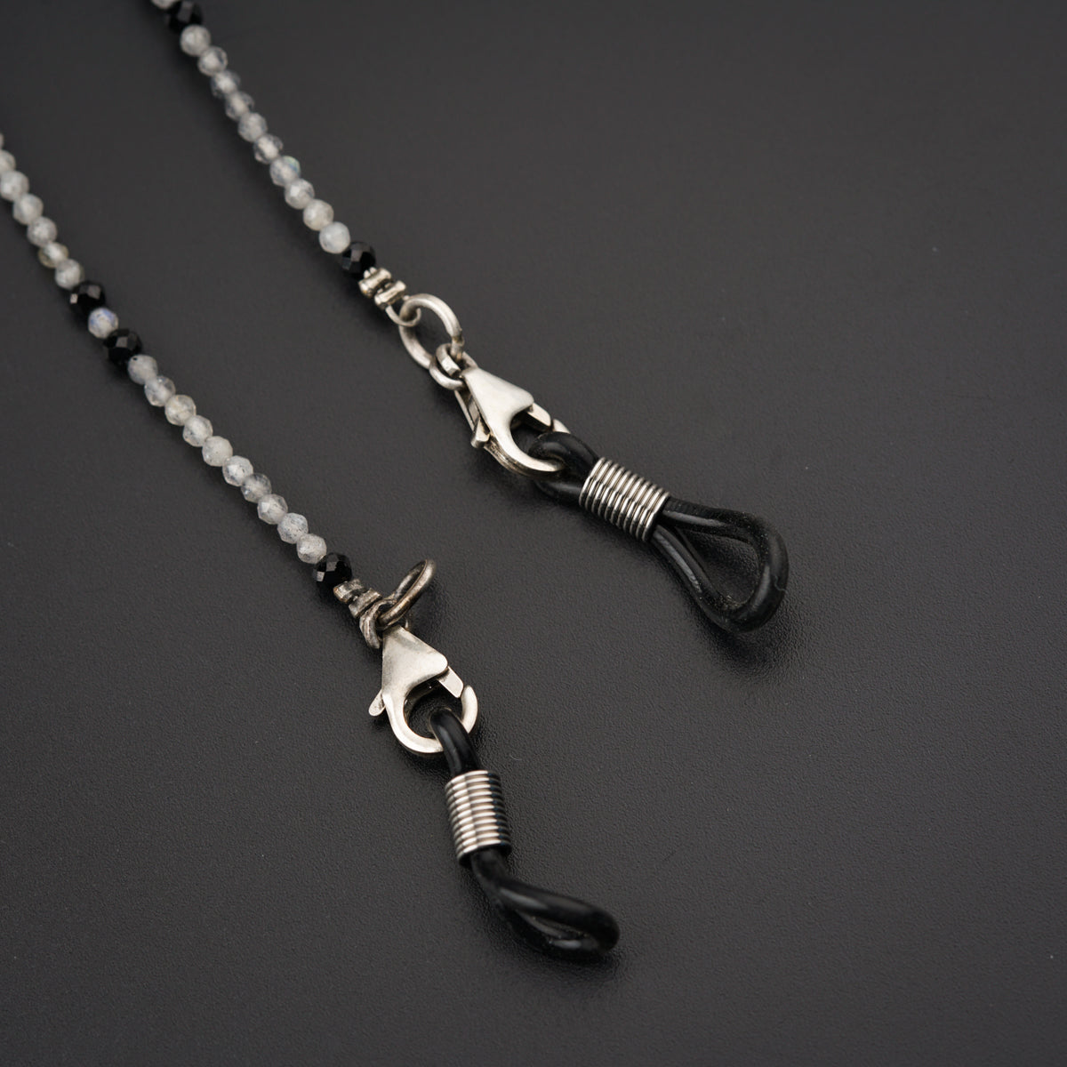 a couple of black and silver necklaces on a black surface