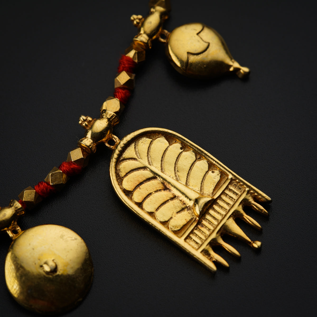a gold necklace with a red beaded cord