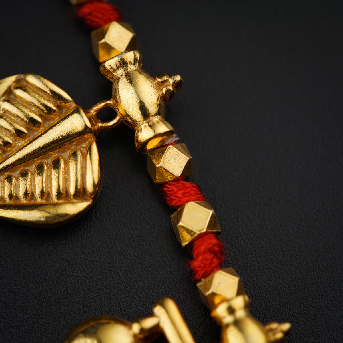 a gold necklace with a red cord on a black surface