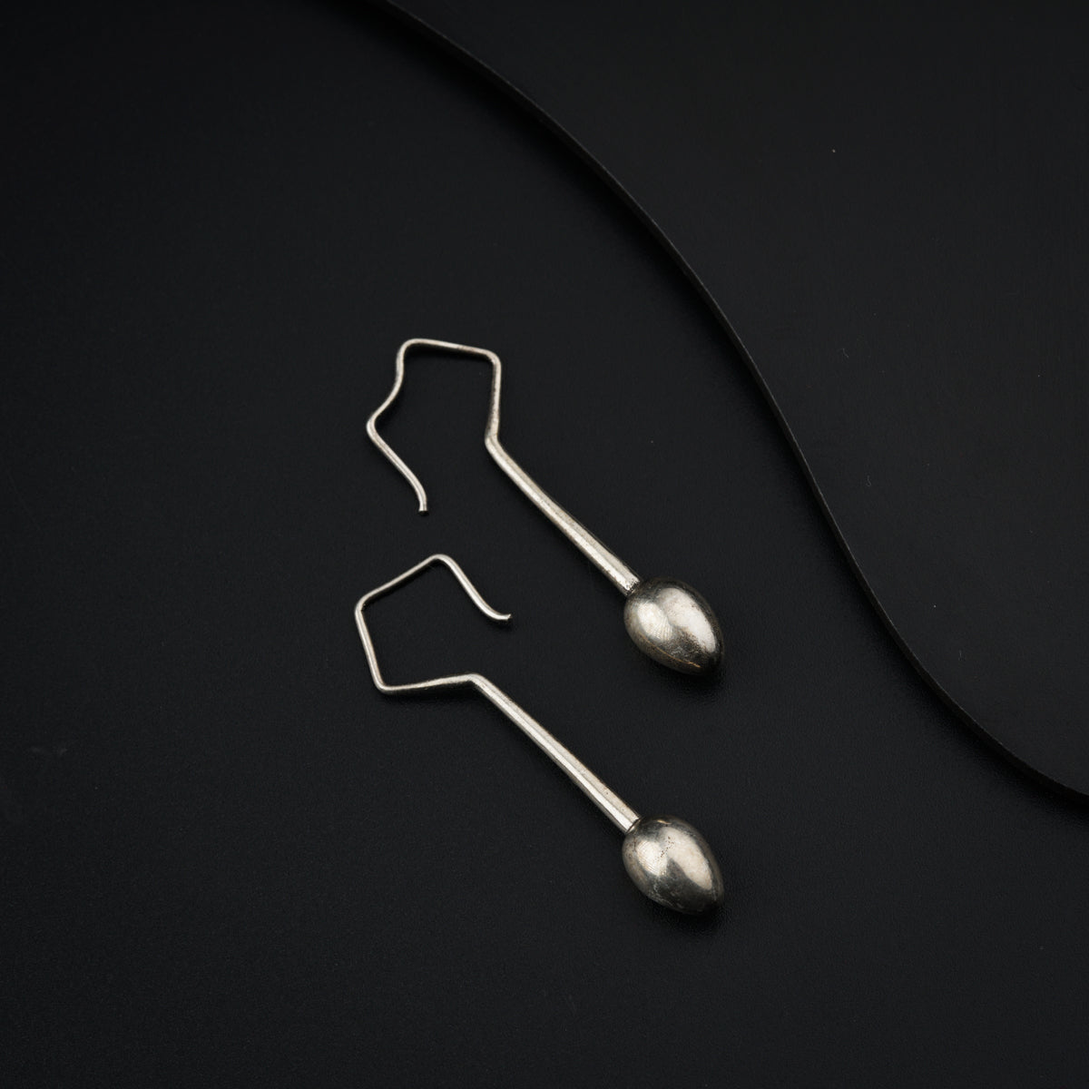 a pair of silver earrings sitting on top of a black surface