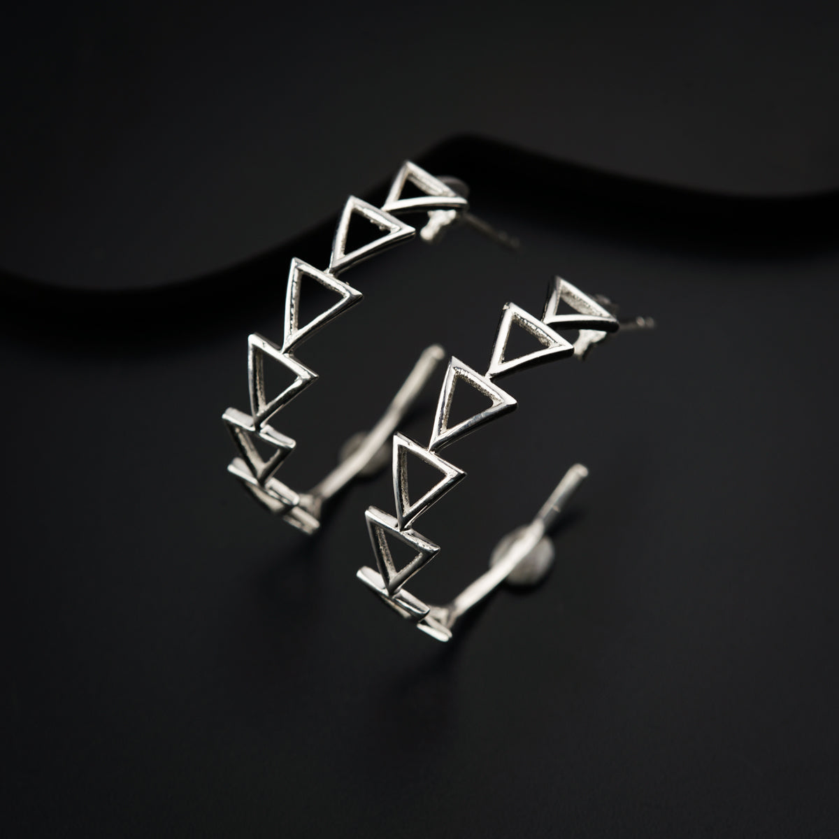 a pair of silver earrings sitting on top of a black surface