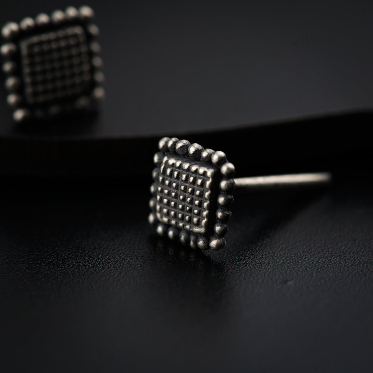 a pair of studded earrings sitting on top of a black surface