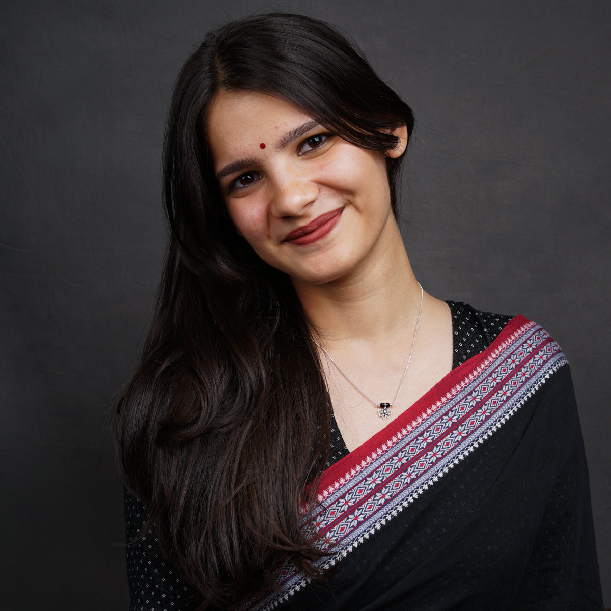 a woman with long dark hair wearing a black and red sari