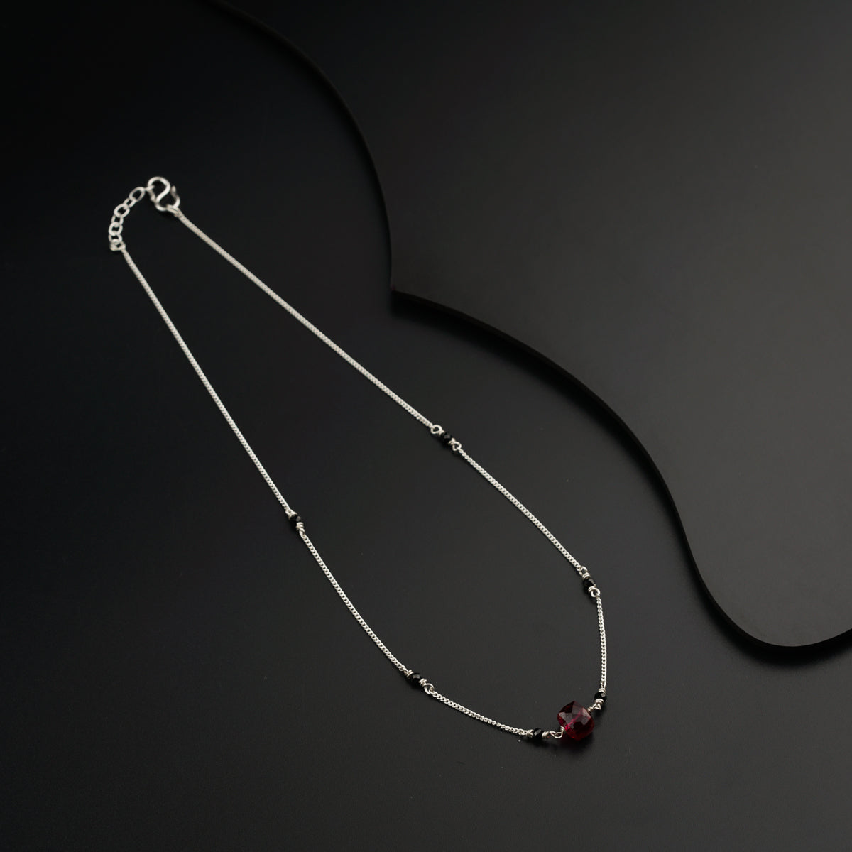 a silver necklace with a red stone on a black background