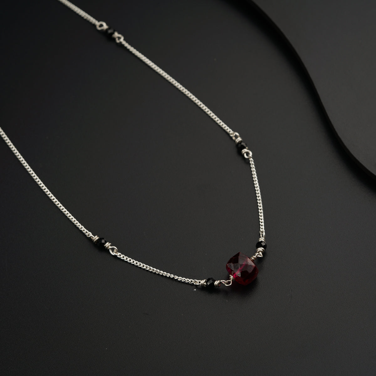 a necklace with a red stone on a black surface