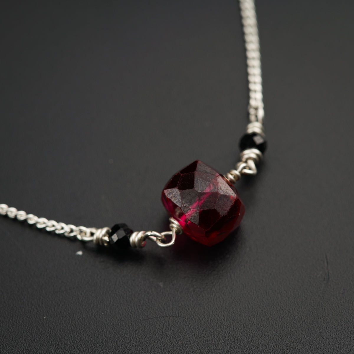 a red necklace with a silver chain on a black surface