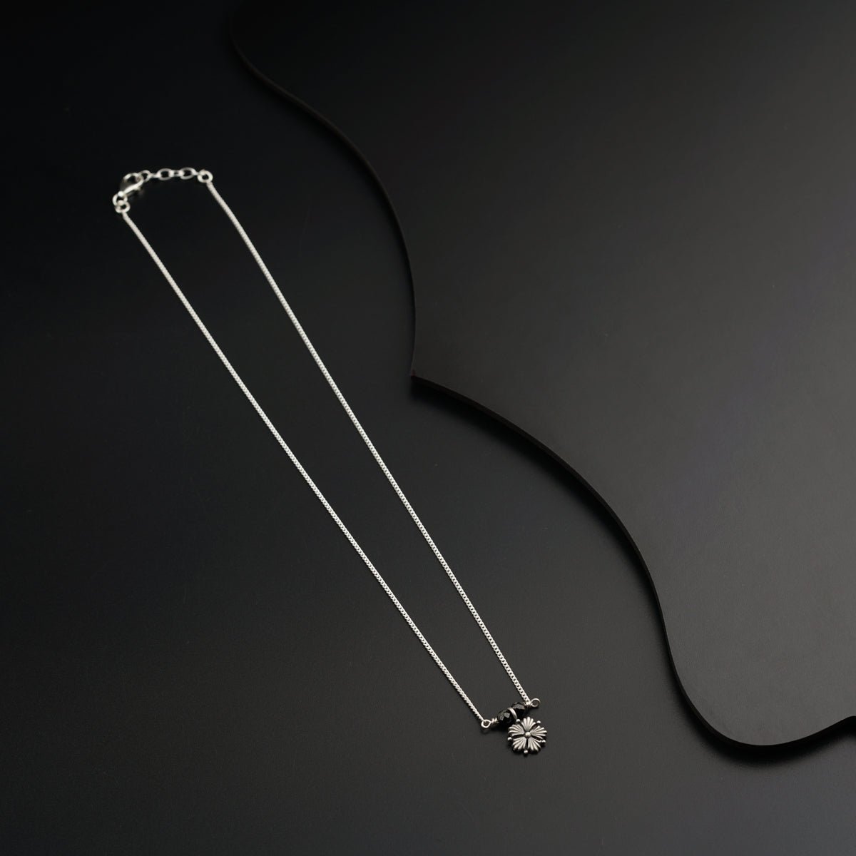 a necklace with a flower on a black background