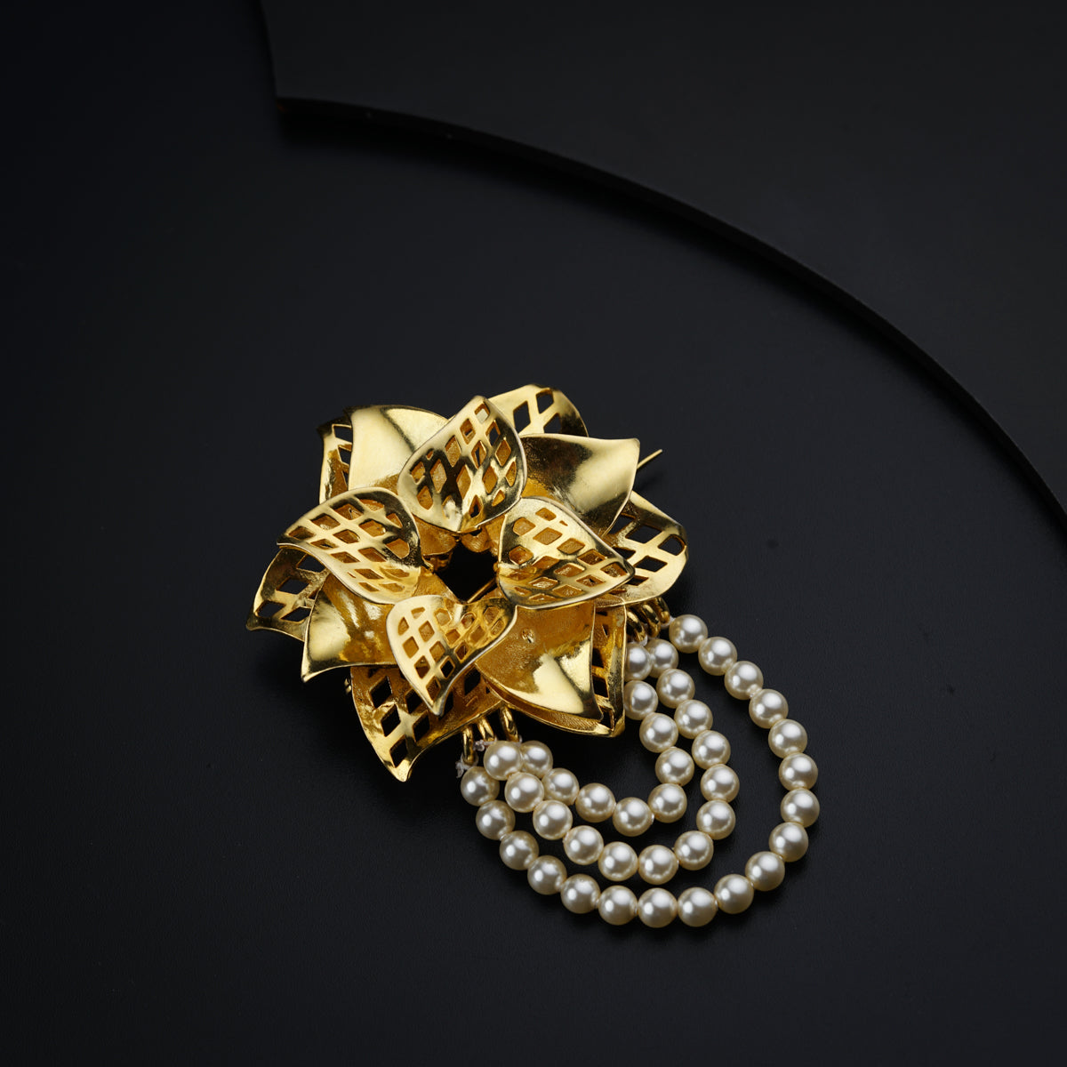 a gold brooch with pearls on a black surface