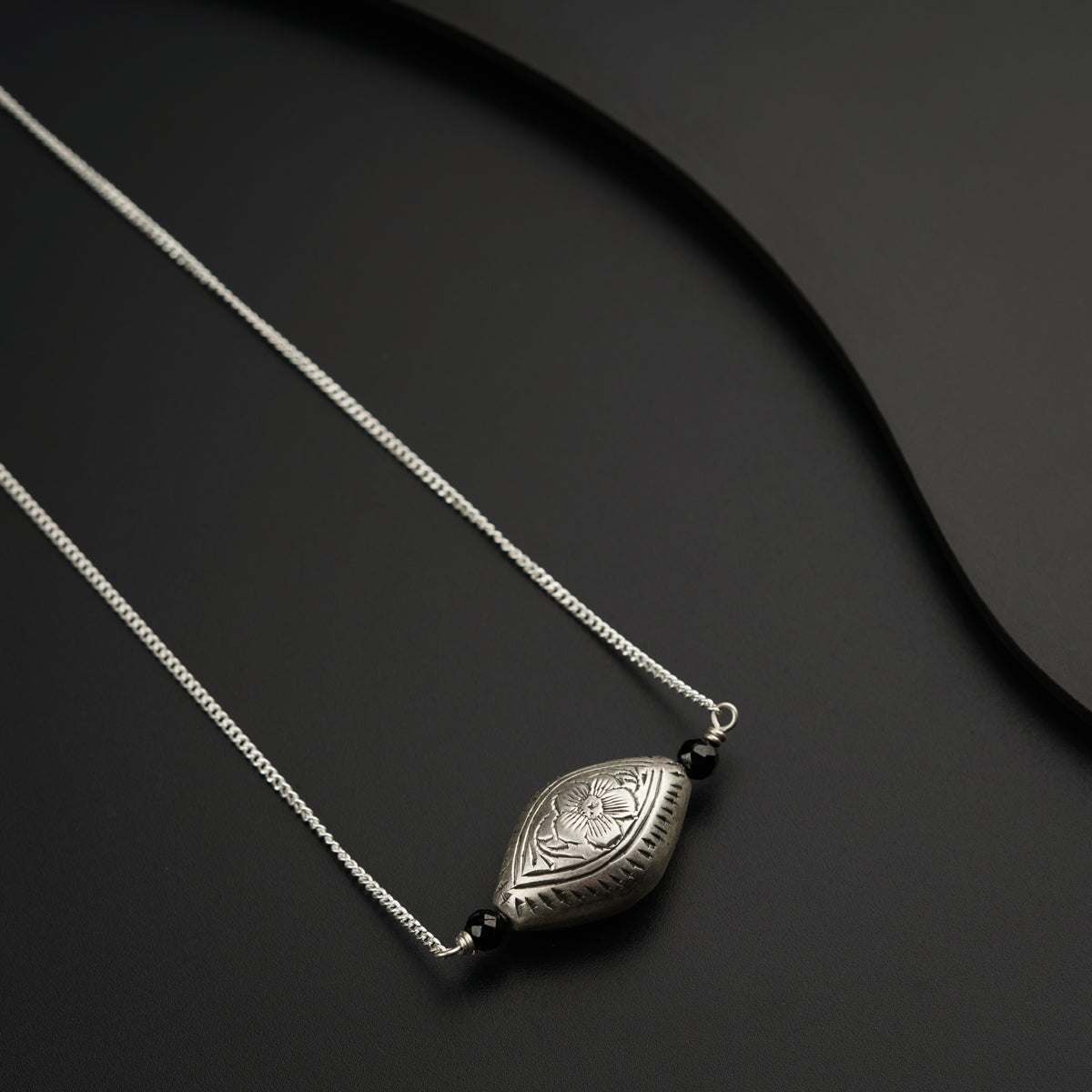 a necklace with a silver pendant on a black surface
