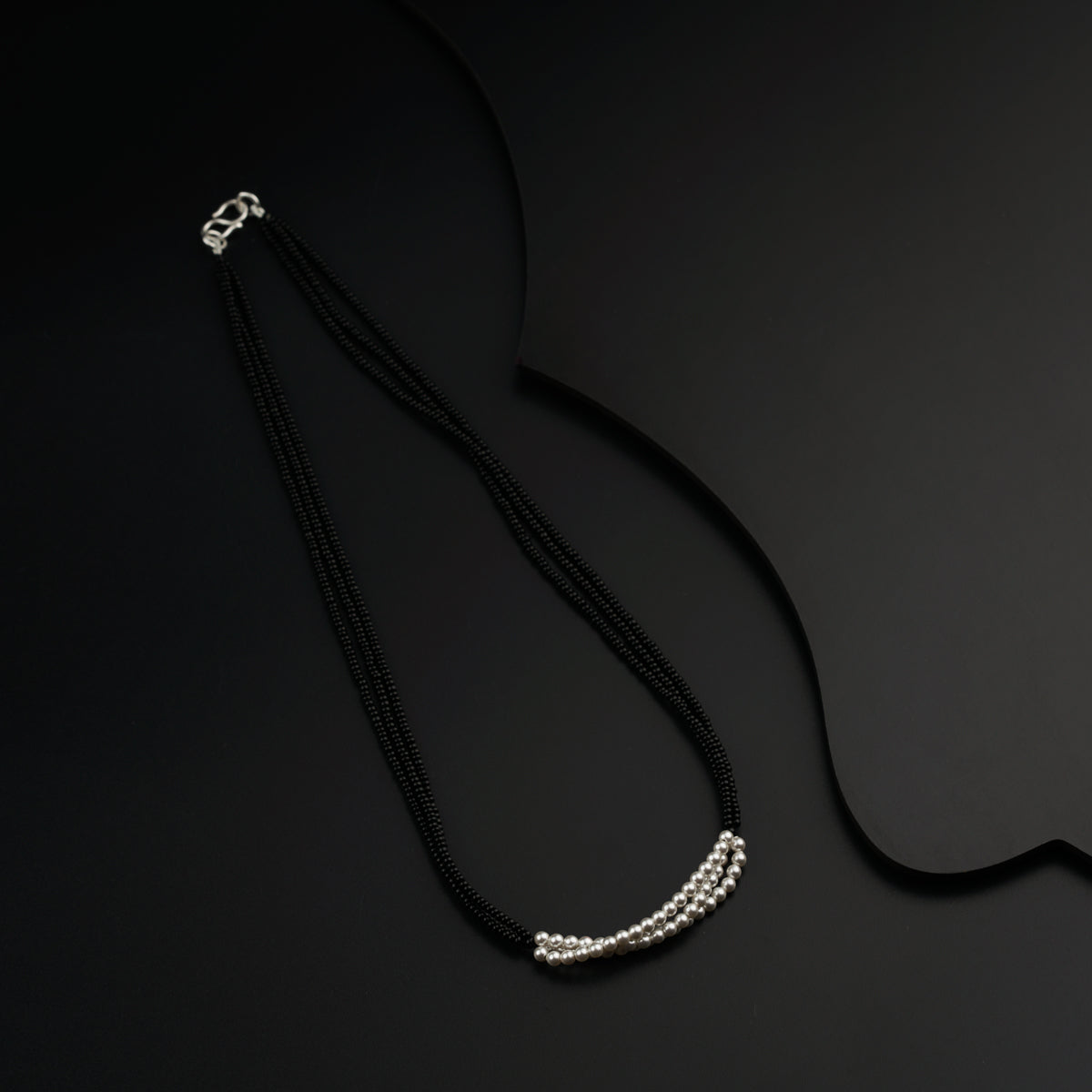 a black necklace with a white bead on a black background