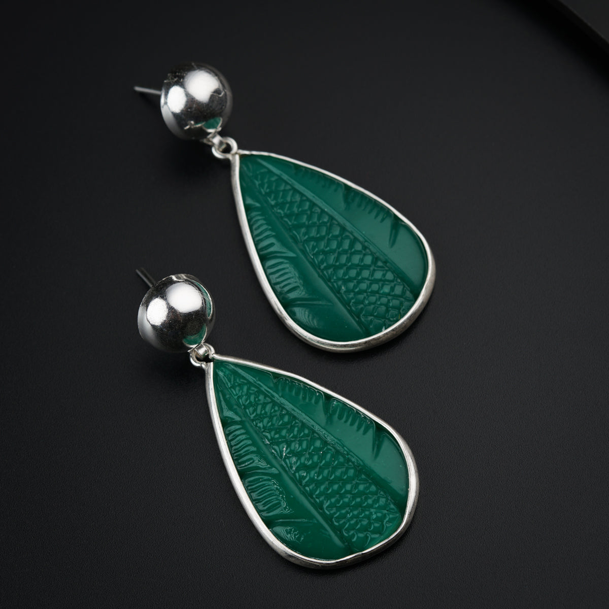 a pair of green earrings on a black surface