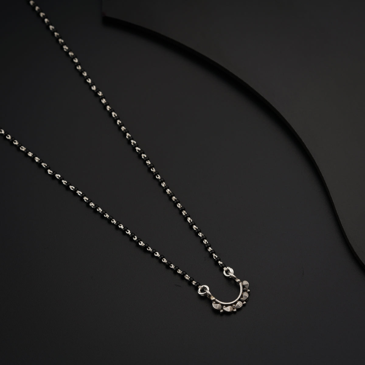 a silver necklace with a circular pendant on a black background