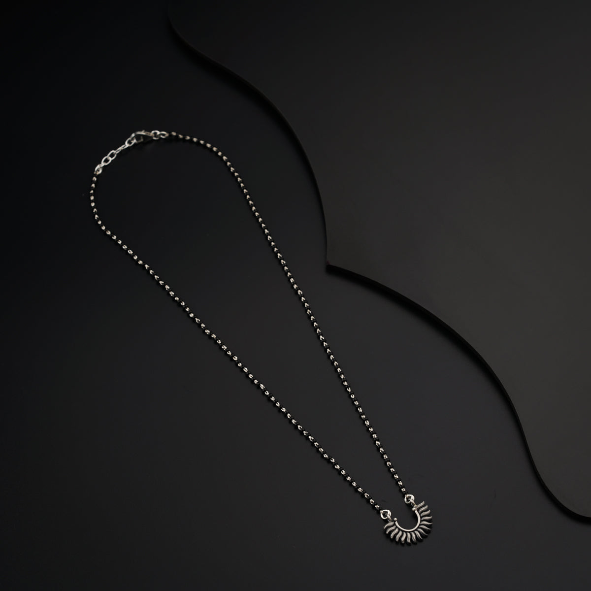 a long necklace with a silver pendant on a black background