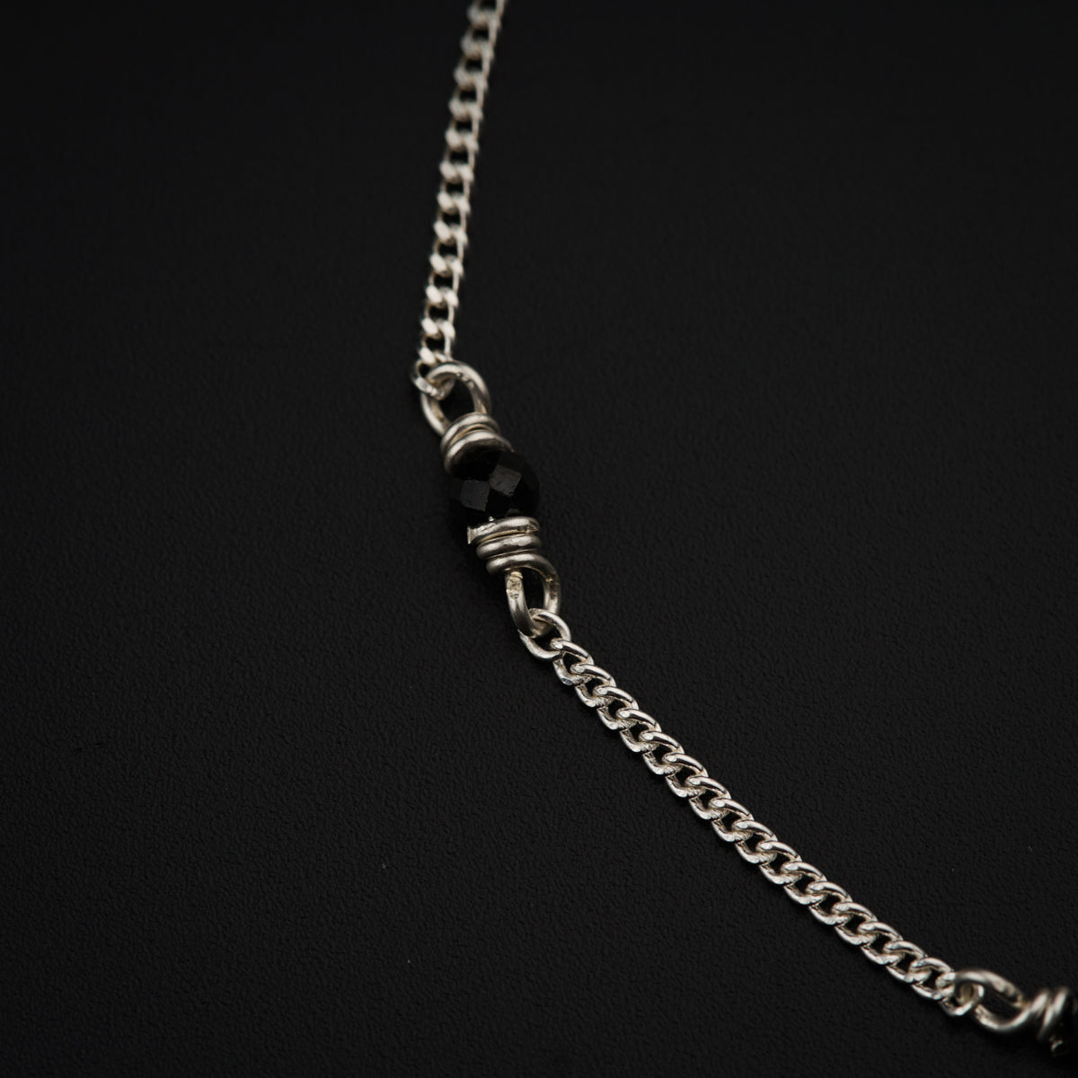 a silver chain with black beads on a black background