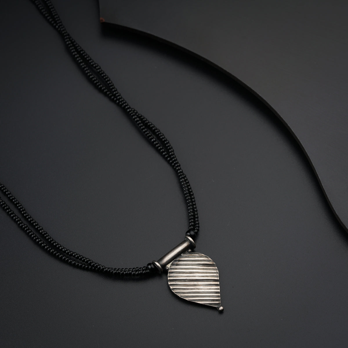 a black cord necklace with a silver pendant on it