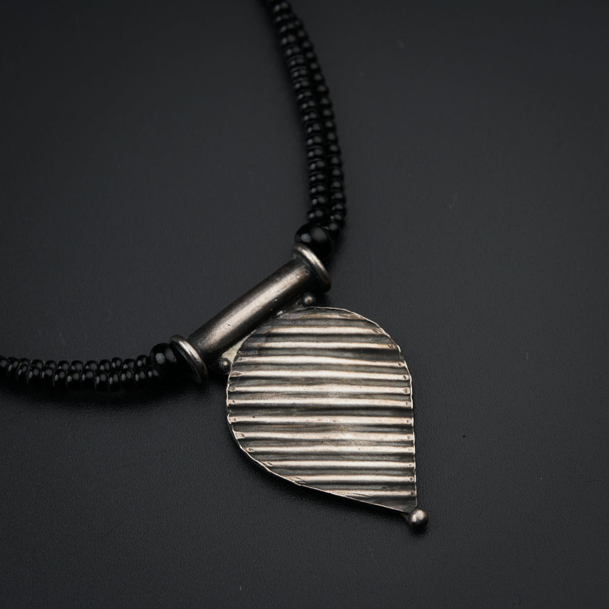 a necklace with a leaf shaped pendant on a black background