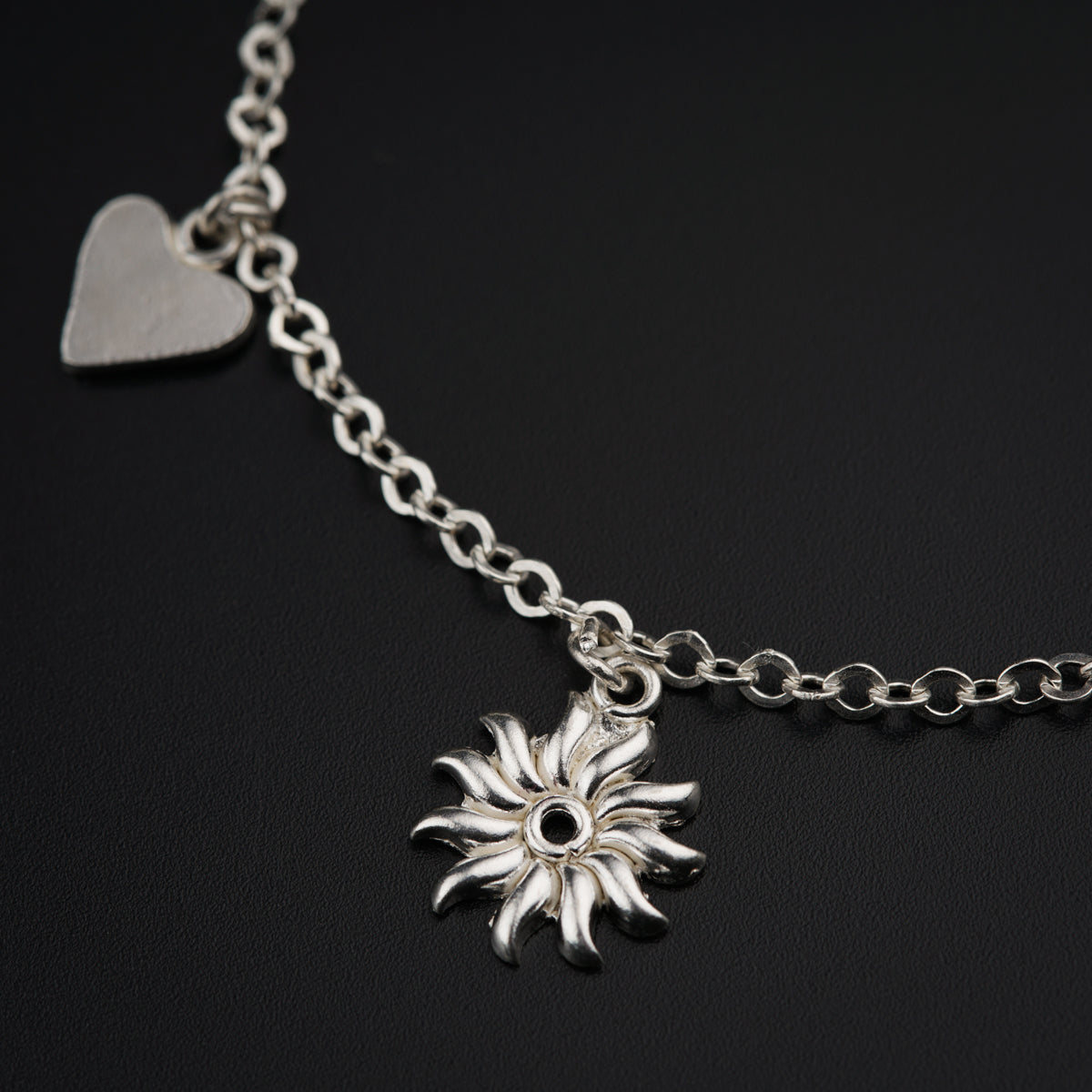 a silver bracelet with a heart and a flower charm