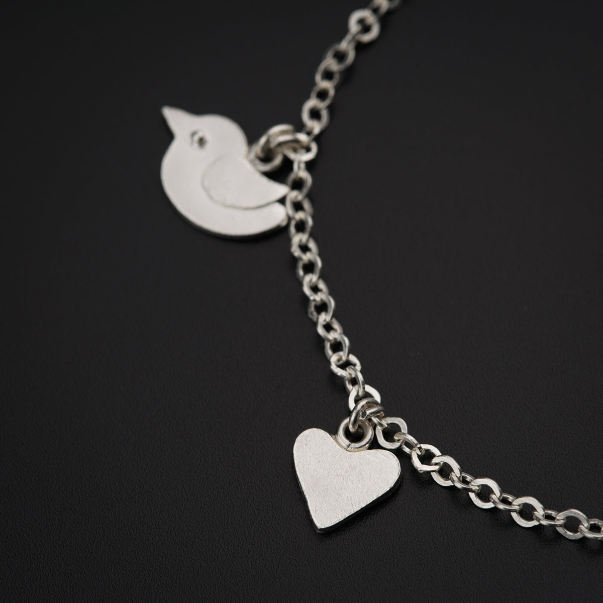 a silver bracelet with a heart and a bird on it