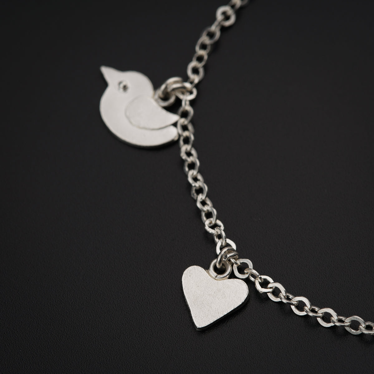 a silver bracelet with a heart and a bird on it