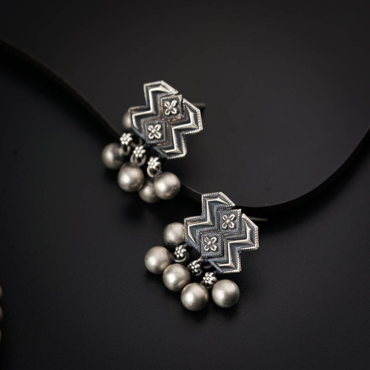 a pair of silver earrings with pearls on a black background