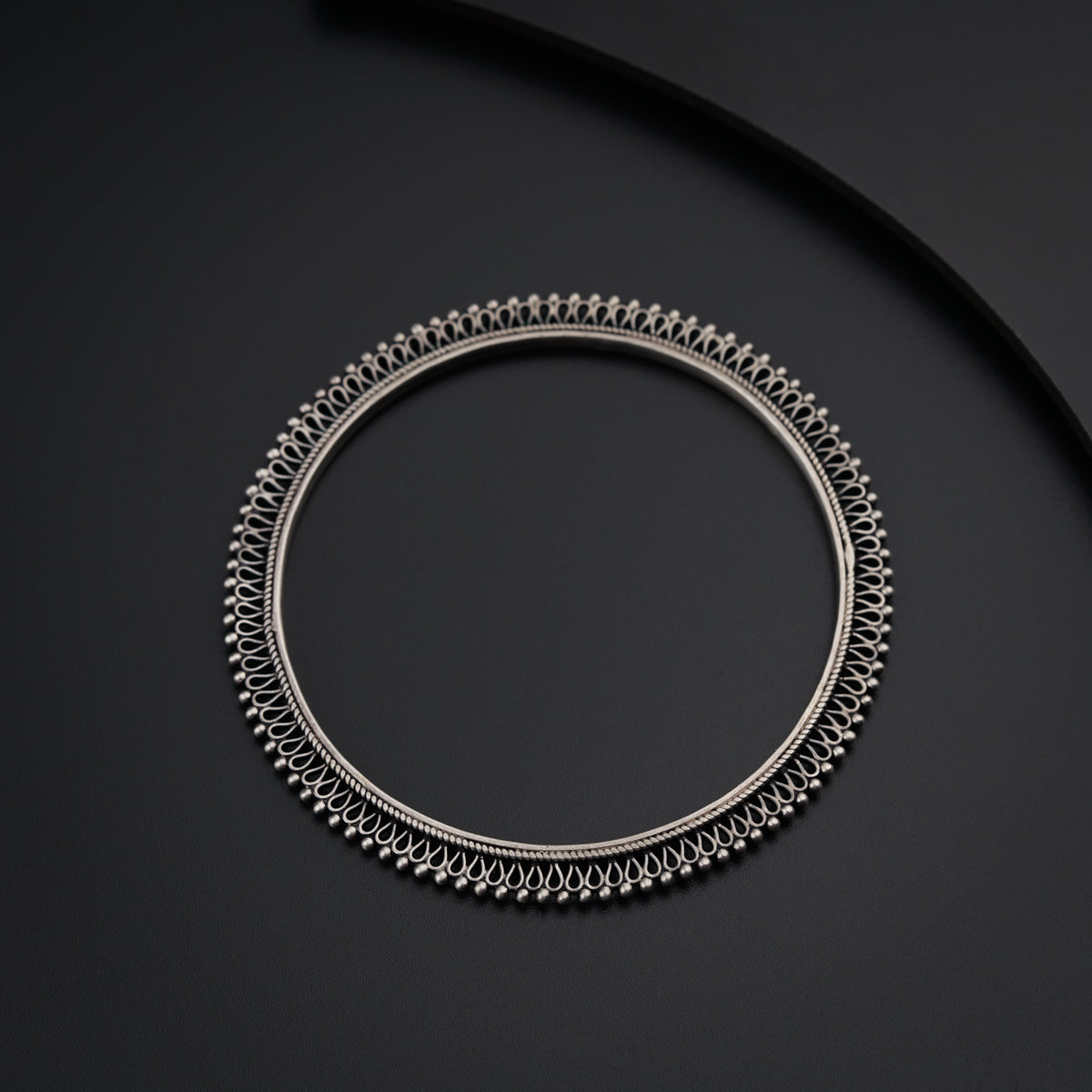 a silver bracelet with a black cord on a black surface