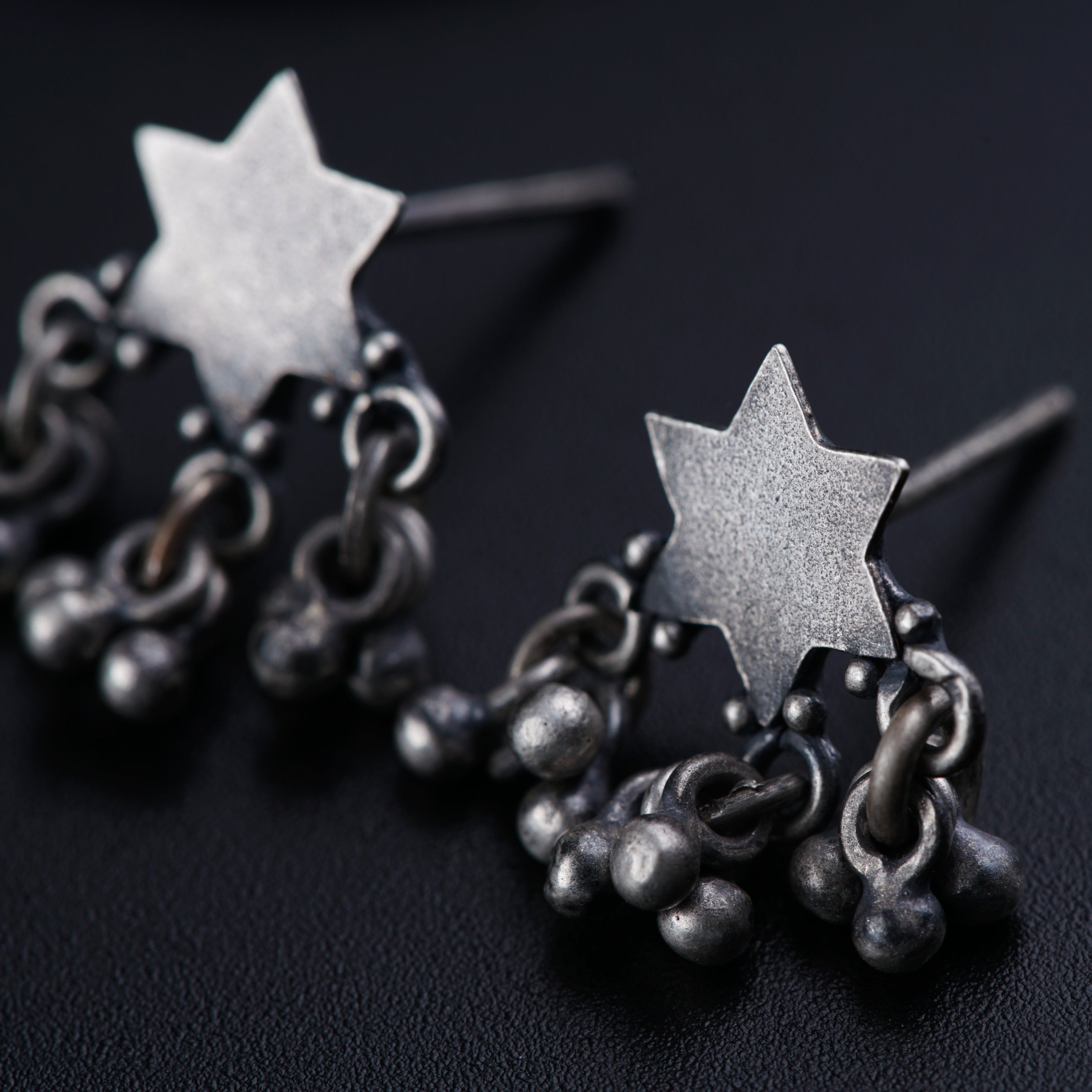 a pair of star and chain earrings on a black surface
