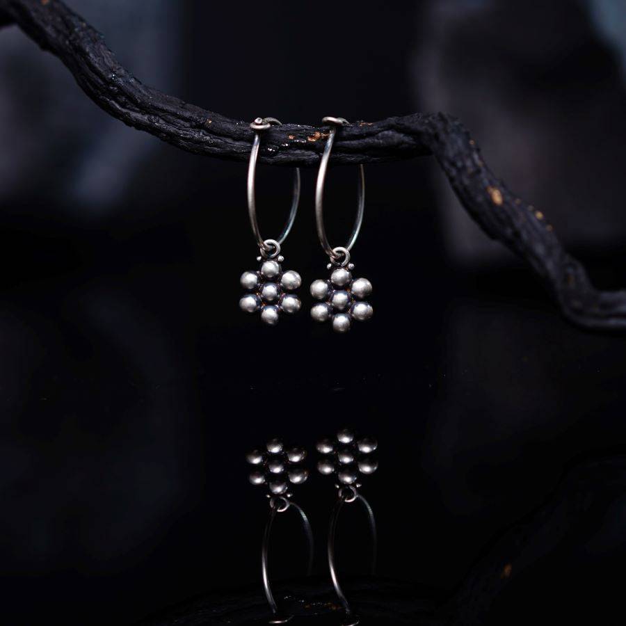 a pair of silver earrings hanging from a tree branch
