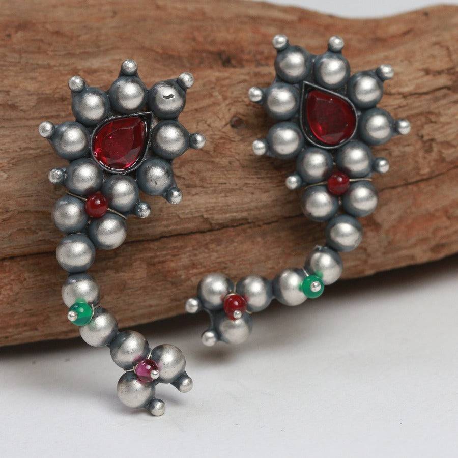 a pair of silver and red earrings sitting on top of a piece of wood