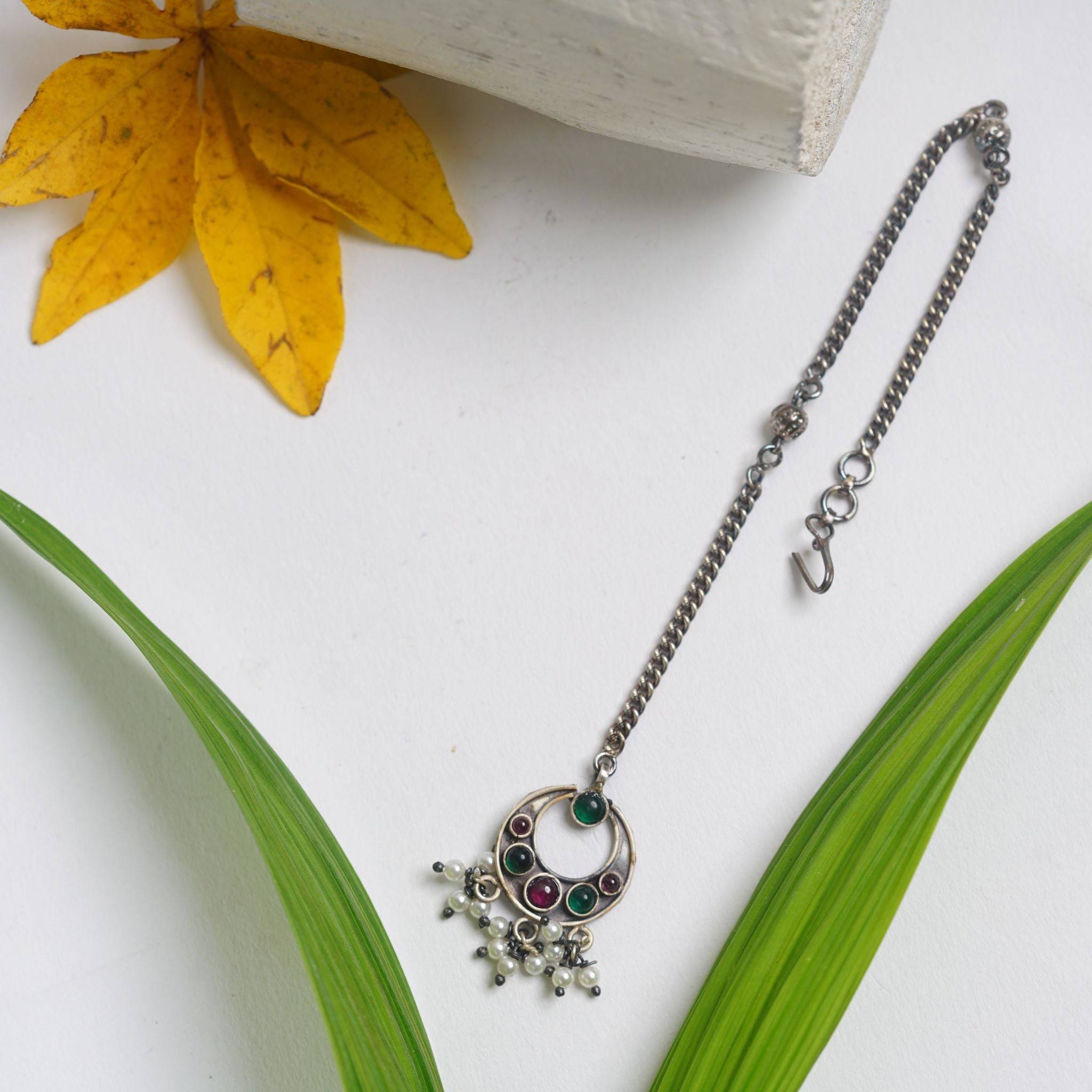 a necklace with a flower on it sitting next to a leaf