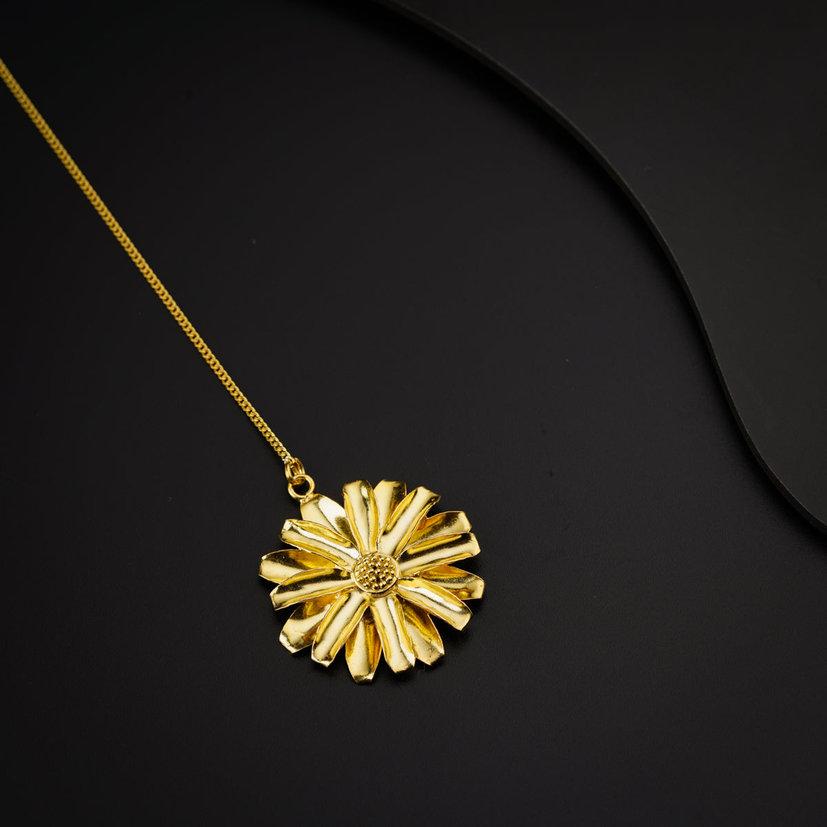 a gold necklace with a flower on a black surface