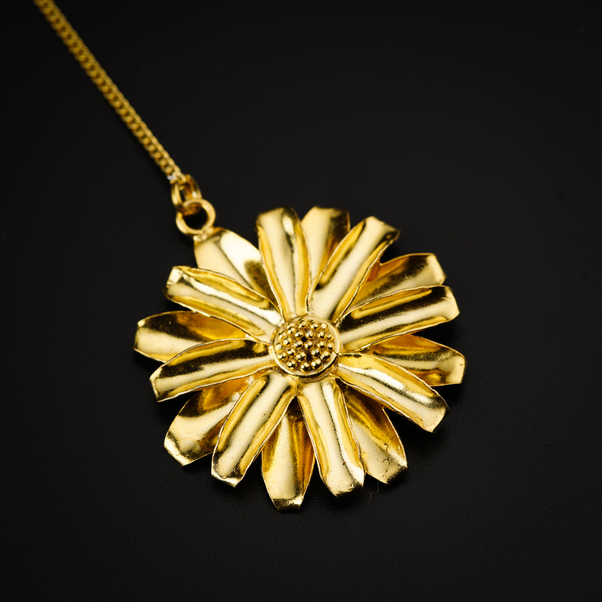 a gold necklace with a flower on a black background