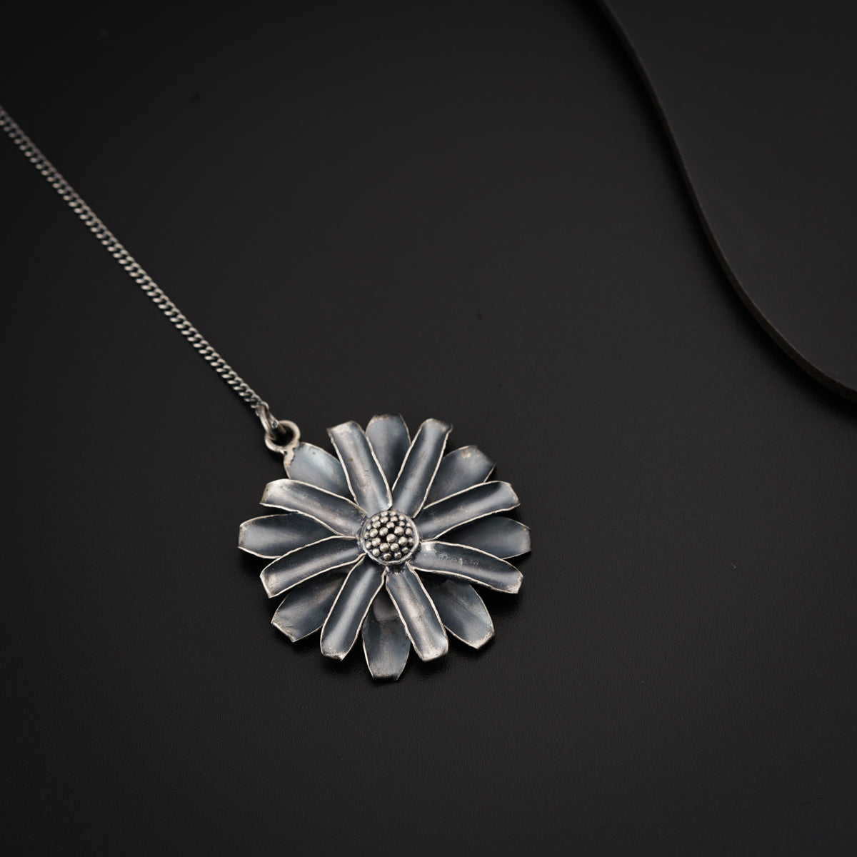 a silver necklace with a flower on a black background