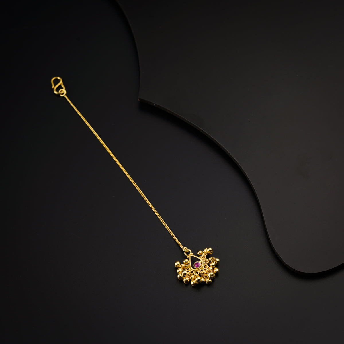 a gold necklace with a red stone on a black background