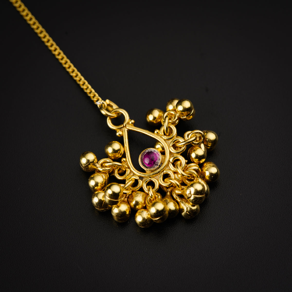 a gold necklace with a red stone in the center