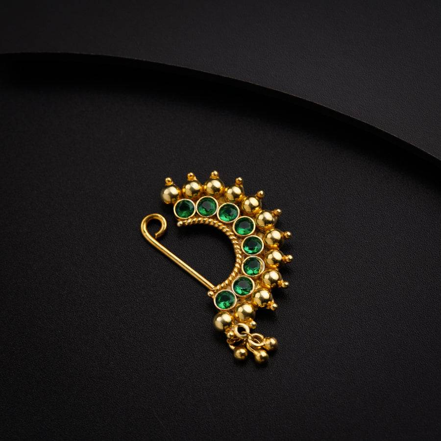 a gold brooch with green stones on a black background
